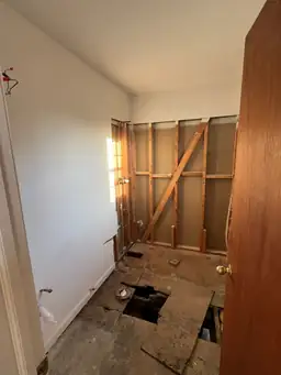Small room during drywall demolition showing exposed pine framing, open subfloor sections, and storm water damage — Marietta, GA