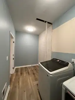 Laundry room after new flooring — LVP hardwood installed, blue painted walls, washer and dryer in place, brick wall accent — Powder Springs, GA
