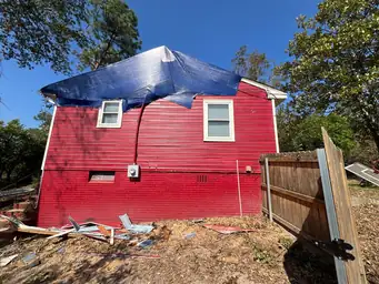 Red two-story home with full blue tarp emergency roof covering and storm debris scattered across front yard — Acworth, GA