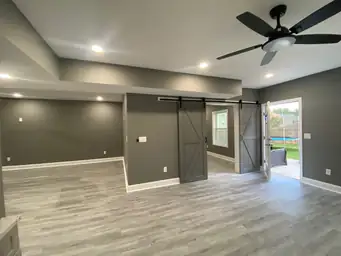 Finished basement living room with gray LVP flooring, charcoal painted walls, dual sliding barn doors, and ceiling fan — Metro Atlanta, GA
