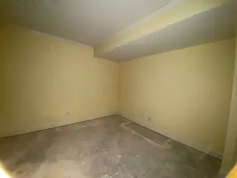 Basement room with pale yellow walls and raw concrete slab exposed after flooring removal during water damage demo phase — Marietta, GA