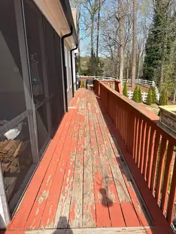 Long side view of peeling faded red deck boards along screened porch wall before deck restoration begins — Marietta, GA