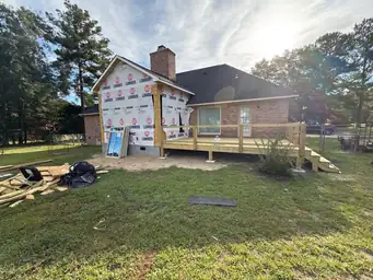 Completed tan fiber cement siding on sunroom addition exterior with large multi-pane windows beside original brick home — Marietta, GA
