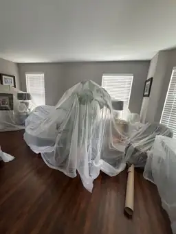 Living room furniture covered in clear protective sheeting during water damage remediation preparation — Smyrna, GA