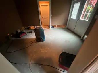 Blue commercial dehumidifier and red air mover on concrete floor with open-stud wall sections removed during basement water damage drying — Marietta, GA