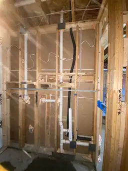 Basement bathroom rough plumbing with white PVC drain stack, supply lines, and black ABS vent pipe in framed wall — Metro Atlanta, GA