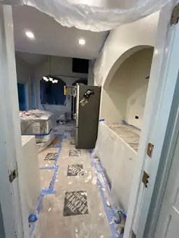 Kitchen renovation during paint prep — plastic sheeting over surfaces, drywall work in progress, arched entry — Powder Springs, GA