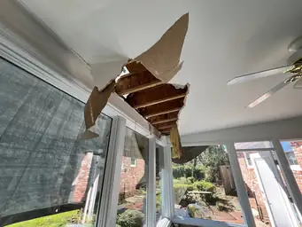 Interior ceiling collapse exposing wood roof decking and rafters with torn drywall hanging over sunroom windows — Marietta, GA