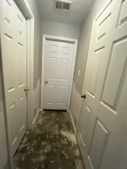 Hallway with multiple white doors and visible drywall patches, showing signs of ongoing construction or restoration work — serving Dallas, GA.