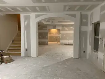Basement finishing with drywall columns flanking curved archway opening and staircase rough framing visible — Atlanta, GA