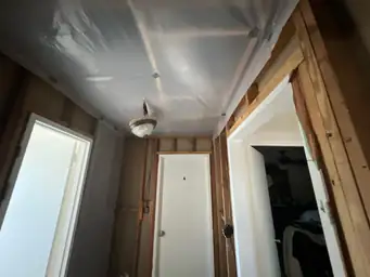 Interior hallway with storm-damaged ceiling fully tarped in plastic sheeting, exposed wood stud walls on both sides — Acworth, GA
