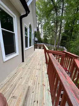 New pressure-treated deck boards awaiting stain beside existing red-painted railing showing deck repair progress — Marietta, GA