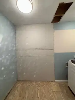 Laundry room during renovation — new drywall installed on wall, ceiling opened for rough-in, subfloor exposed — Powder Springs, GA