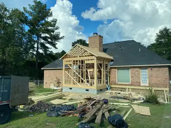 Close exterior view of sunroom addition gable framing on CMU block foundation with partial deck beside brick home — Marietta, GA