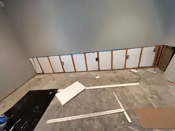 Partial wall demolition with exposed studs and electrical outlets, materials and tools on the floor — serving Dallas, GA.