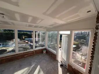 Wide view of sunroom water damage repair with new drywall ceiling seams and stripped brick walls visible — Marietta, GA