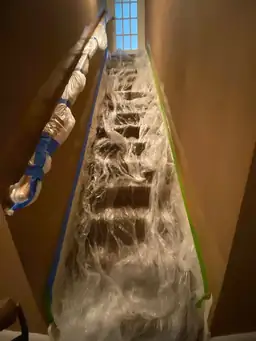 Basement staircase wrapped in clear plastic with blue and green tape edge sealing during containment for water damage remediation — Marietta, GA