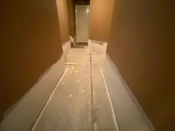 Basement hallway with bare concrete subfloor and tan walls showing new white baseboard trim installed during water damage restoration — Marietta, GA