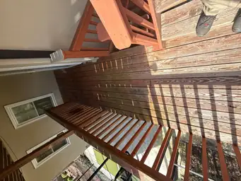 Overhead view of dark brown stain freshly applied to repaired deck boards with red-painted stair railings visible — Marietta, GA