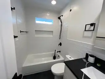 Finished bathroom remodel with white subway tile tub surround, matte black fixtures, white vanity, and dark slate floor tile — Marietta, GA