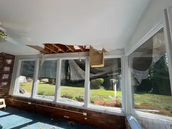 Sunroom ceiling collapse with torn white drywall exposing roof framing above windows before water damage repair — Marietta, GA