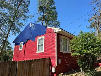 Red two-story home exterior showing blue tarp emergency roof covering secured over storm-damaged roofline — Acworth, GA