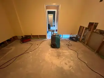 Teal commercial dehumidifier centered on concrete basement floor with removed lower wall drywall during water damage mitigation — Marietta, GA