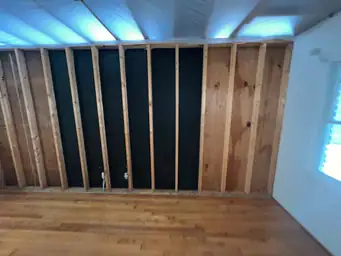 Stripped interior corner showing bare wood studs and poly ceiling barrier during drywall demo after storm damage — Marietta, GA
