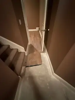 Basement hallway with damp bare concrete and water-stained trim strip at base of stairs during water damage mitigation — Marietta, GA