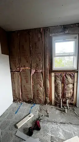 Stripped interior wall revealing R-13 fiberglass batt insulation in wood stud framing during storm damage remediation — Acworth, GA