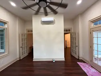 Sunroom addition interior with dark hardwood floor and mini-split unit during exterior siding installation phase — Marietta, GA