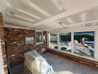 Sunroom during storm restoration with new drywall ceiling, covered furniture, and exposed brick perimeter walls — Marietta, GA