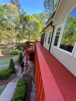 Deck staining in progress on new pressure-treated boards with partial red coverage beside home and landscaping — Marietta, GA
