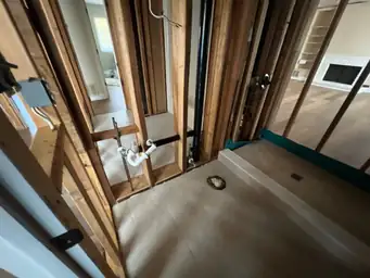 Bathroom wall opened during storm water damage demolition revealing pine studs, supply lines, and P-trap plumbing — Kennesaw, GA