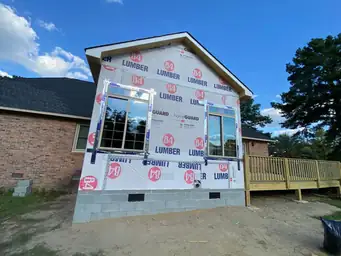 Sunroom addition mid-construction with 84 Lumber house wrap on gable, two windows installed, and CMU block foundation — Marietta, GA