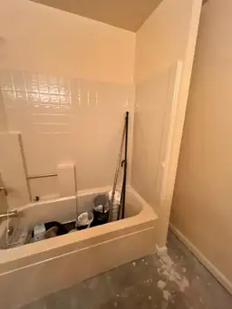 Bathroom renovation showing a tub filled with cleaning tools and materials, with partially finished flooring — serving Dallas, GA.