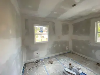 Interior room drywall finishing during home renovation with skim-coated walls, two windows, and construction debris — Marietta, GA