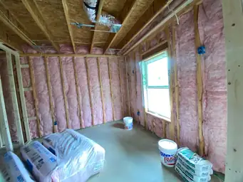 Basement insulation phase with pink fiberglass batts in stud walls, joint compound buckets staged for finish phase — Metro Atlanta, GA