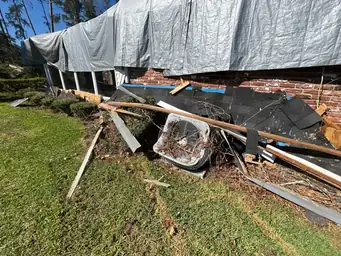 Storm-torn roof edge with scattered shingles, lumber debris, and grey tarp over damaged brick structure — Marietta, GA