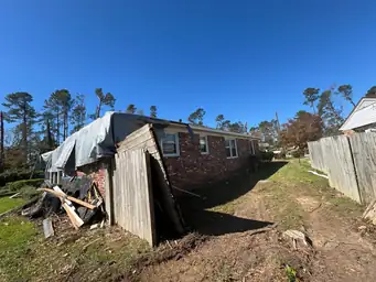 Side-yard view of brick home after storm with collapsed outbuilding and full-coverage grey roof tarp installed — Marietta, GA