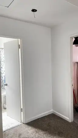 Interior bedroom corner with bare drywall, exposed ceiling fixture wiring, and restoration equipment in doorway — Acworth, GA