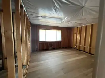 Wide room with all walls stripped to studs, poly ceiling, and new light plank flooring after water damage remediation — Kennesaw, GA