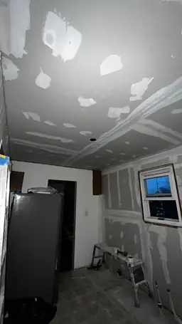 Kitchen ceiling and walls covered in fresh drywall with joint compound patches, ladder and mud bucket on site — Acworth, GA