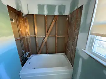 Bathroom water damage remediation with stripped studs surrounding white porcelain tub and new green moisture-resistant drywall — Marietta, GA