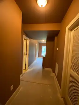 Long basement hallway with brown painted walls and raw concrete subfloor stripped before flooring replacement during water damage restoration — Marietta, GA