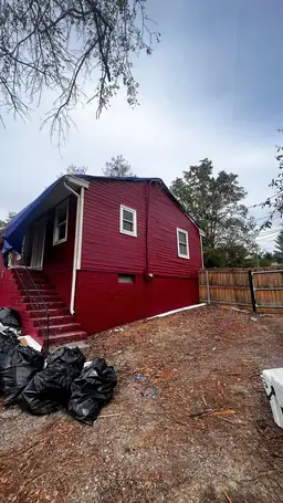 Red two-story home exterior with emergency blue tarp on roof, storm debris piled in yard, and detached garage — Acworth, GA