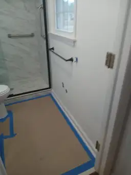Bathroom during restoration with blue painter tape protecting floor around new marble-tile shower enclosure — Marietta, GA