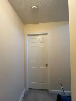 Image of a hallway under construction with a closed door, textured ceiling, and unfinished flooring — serving Dallas, GA.