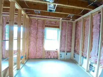 Basement bedroom framing with pink fiberglass batt insulation filling stud cavities, HVAC box vent rough-in overhead — Metro Atlanta, GA
