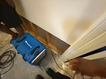 Interior scene with an exposed wall section and a blue dehumidifier on the floor during water mitigation — serving Dallas, GA.